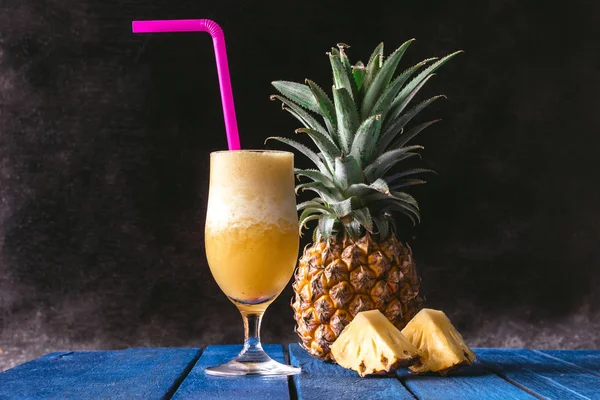 Pineapple smoothie and Fresh Pineapple fruit on blue wooden table with black background.