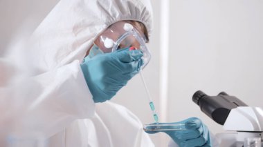 PPE süitindeki bilim adamı laboratuardaki bir deney tüpünde sıvı kontrolü yapıyor..