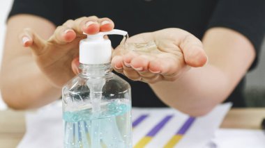 İş kadını masasında çalışırken dezenfektan alkolle el temizliği yapıyor..