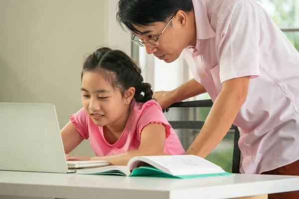 Father is teaching his daughter to do homework during online distance learning at home.