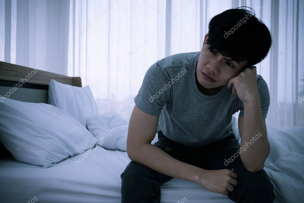 Stressed Asian young man sitting alone on bed. Bad relationship or bankrupt problem and sickness concept.