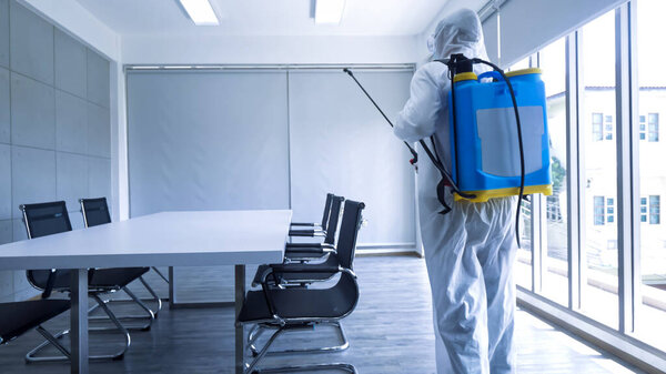 Worker in personal protective equipment (ppe) suit cleaning in building with spray disinfectant water to remove covid 19