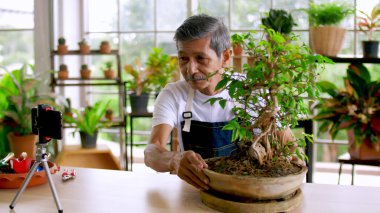 Senior gardener man selling beautiful plants on social media by streaming live from his shop. clipart