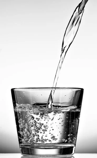 Pouring water into a glass cup on white background. Black and white.