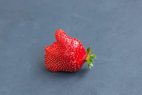 Unusual fresh organic strawberries. Like symbol (Thumb up). Red juicy berry on a blue background, copy space. Concept - Eating ugly fruits and vegetables.