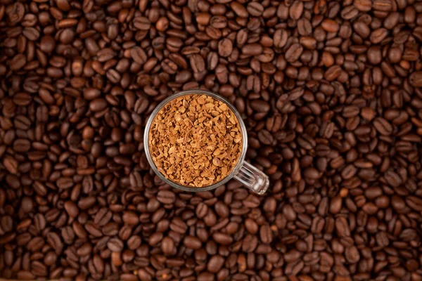 Instant, freeze-dried or granulated coffee in a transparent cup on the background of roasted coffee beans. Used to make a cold Dalgon coffee drink. Selective focus. Top view.
