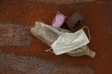 Pis pislik. Paslı metal arka planda çürüyen atıkların toplanması. Kullanılmış yüz maskeleri çevreyi kirletir. Koronavirüs salgınının sonucu olarak yeni bir çöp türü ortaya çıktı..