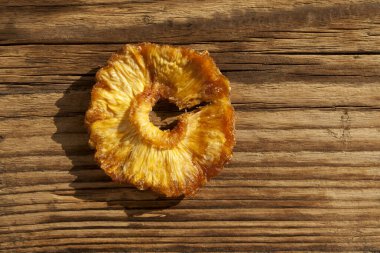 Kurutulmuş ananas. Yuvarlak bir dilim eski kahverengi bir tahta üzerinde yatar. Şekersiz sağlıklı doğal tatlılar. Üst görünüm, alanı kopyala.