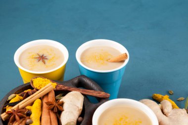 Hint Masala çayı (Masala çayı) ya da malzemelerin yanında bulunan çok renkli seramik bardaklarda bulunan altın süt. Seçici odak, boşluğu kopyala.