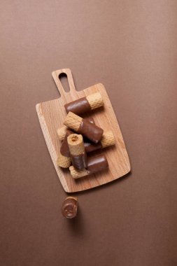 Kahverengi arka planda tahta servis tahtasının üzerinde yarım kaplamalı sütlü gofret ruloları. Üst görünüm, alanı kopyala.