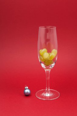 Köpüklü şarap için bir kadehte 12 üzüm. Seçici odak, kırmızı arkaplan, kopyalama alanı. İspanyol geleneklerine göre 12 böğürtlen yemek gece yarısında iyi şans getirir. Yeni yıl kompozisyonu.