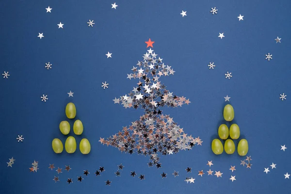 Mavi arka planda yıldız ve üzüm şeklinde pullardan yapılmış Noel ağacı. Seçici odaklanma. Gece yarısında şans getirmesi için 12 dut yemek İspanyol geleneğidir. Yeni yıl kompozisyonu.