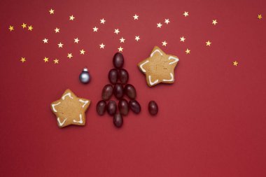 Alternatif Noel ağacı üzümlerden ve kırmızı arka planda Noel kurabiyelerinden yapılmış ve boşluğun bir kopyası var. Yılbaşı geleneği gece yarısı iyi şans için 12 üzüm yemektir..