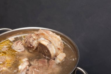 Ev yapımı sığır eti çorbası koyu arka planda bir tencerede pişirilir. Kemikler, vücuda proteinlerin yapı taşları olan amino asitleri sağlayan kolajen içerir. Yakın çekim, seçici odaklanma.