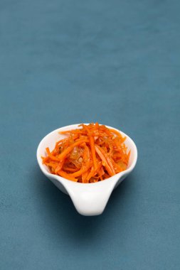 Kore usulü baharatlı ve sarımsaklı Asya havuç salatası. Yakın plan, seçici odaklanma. Mavi arka planda Kore yemekleri.