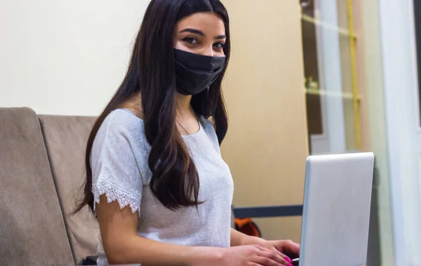 young woman on protective mask working on laptop, businesswoman on protective mask working on laptop in office, young businesswoman in office