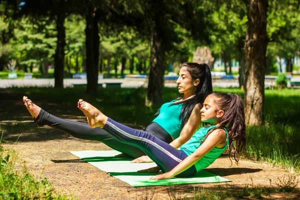 young mother and daughter doing yoga exercises, young woman doing yoga exercises in the park, mother and daughter doing yoga