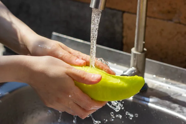 hands of woman washing a green pepper in kitchen