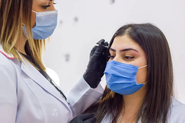 young cosmetologist with a medical mask working on his client