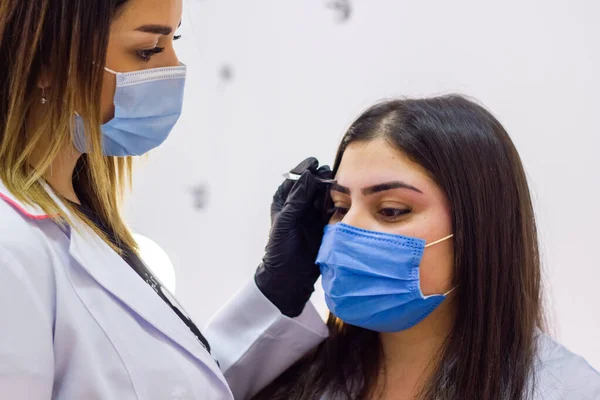 young cosmetologist with a medical mask working on his client