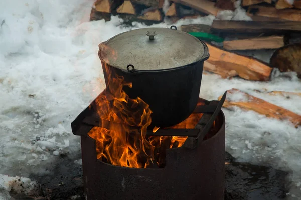 The soup is cooked in a large pot over a fire.