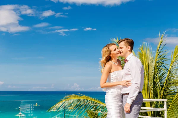ホテルの屋上の新郎新婦は白いウェディング ドレスで美しい金髪の花嫁 バック グラウンドで熱帯の海とヤシの木 夏の休暇の概念 — ストック写真