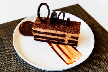 Masanın üzerinde beyaz bir tabakta servis edilen bir parça çikolatalı pasta. Kapatın. Lezzetli atıştırmalıklar ya da bir dilim kek ile kahve zamanı..