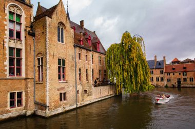 Bruges, Flanders, Belçika, Avrupa - 1 Ekim 2019. Eski tuğlalardan ve Bruges 'ün sonbaharında kanallardan geçen turist teknelerinden yapılmış ortaçağ antik evleri (Brugge)