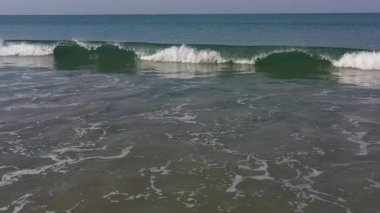 Sakin denizden dalgalar mavi gökyüzünün altında kumlu sahilde kırılıyor