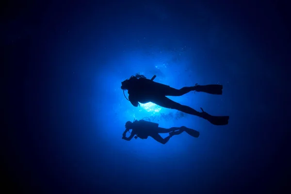 青い海の奥に潜るダイバーのグループの水中写真 — ストック写真