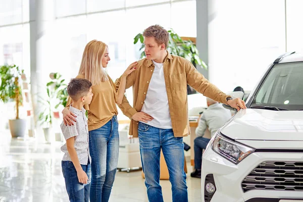 Belo casal caucasiano posando na câmera ao lado de novo automóvel na concessionária — Fotografia de Stock