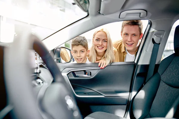 Mladá bělošská rodina se dívá dovnitř auta a prohlíží si ho — Stock fotografie