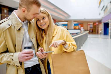 Şık bir çift alışveriş merkezi koridorunda akıllı telefon kullanır.