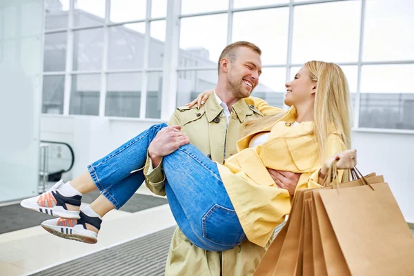 Veselý muž držet veselou ženu v rukou po nakupování — Stock fotografie