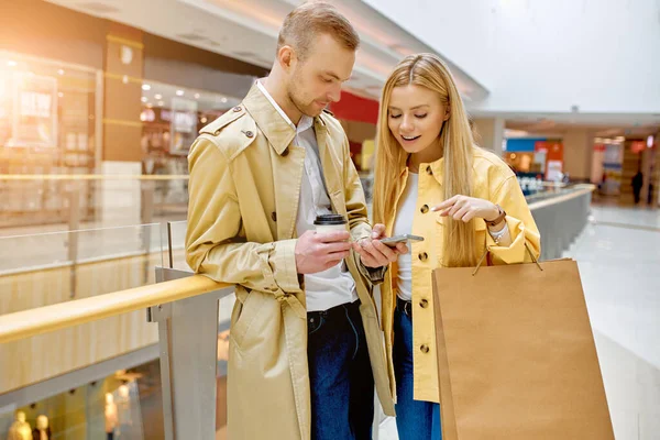 时尚情侣在商场的过道上使用智能手机 — 图库照片