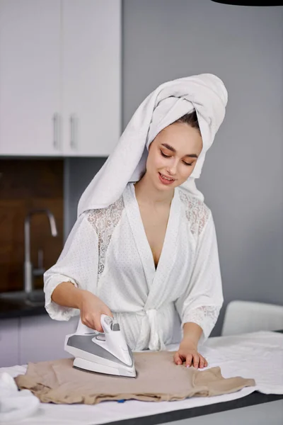 Улыбающаяся красивая женщина тщательно гладит одежду — стоковое фото