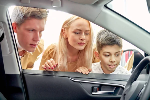 Young caucasian family look inside of car, inspecting it — Stock Photo, Image