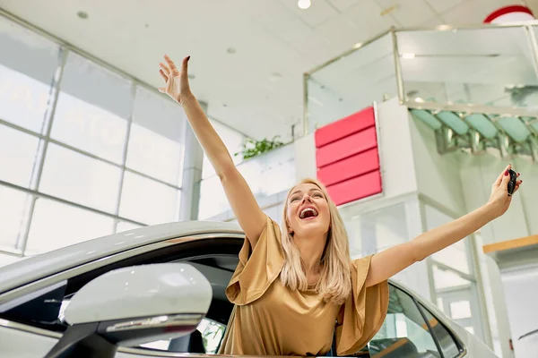 Jovem mulher grita com felicidade dentro do carro na concessionária — Fotografia de Stock