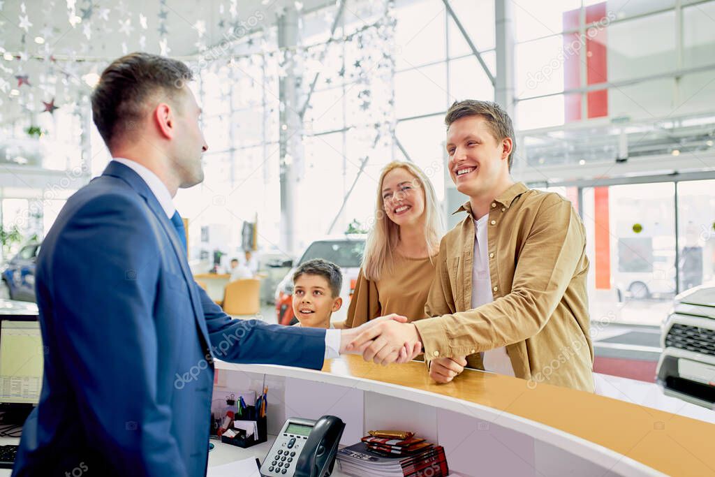 pleasant customers shake hand to responsive consultant of cars dealership