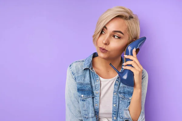 Grappige vrouw met behulp van een schoen als een telefoon houden het in de buurt van haar gezicht en praten — Stockfoto