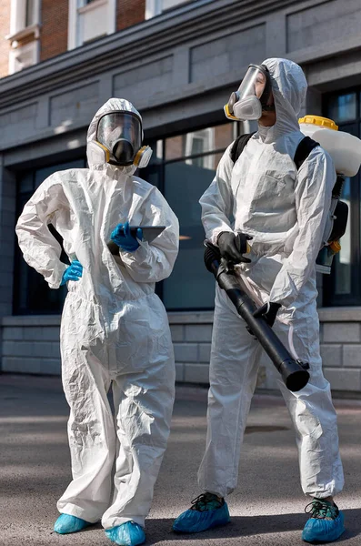 Professional disinfectors in protective hazmat suit walking through city streets — Stock Photo, Image