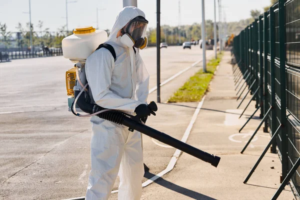 Hombre de traje blanco y protegido con desinfectante limpia las calles —  Fotos de Stock