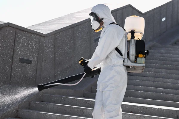 Uomo in tuta bianca completamente protetta con disinfettante pulire le strade — Foto Stock