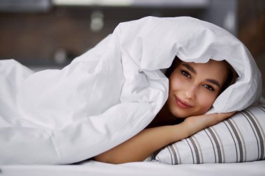 Genç ve güzel bir kadın yatakta yatıyor.