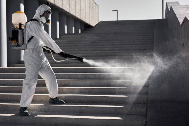 Tehlikeli giysideki genç dezenfektan mikroplu bölgede dezenfeksiyon yapıyor.