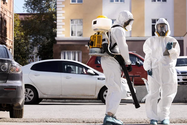 Desinfectantes profesionales en traje protector de materiales peligrosos caminando por las calles de la ciudad —  Fotos de Stock