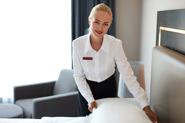 Bautiful maid setting up white pillow on bed sheet in hotel room — Stock Photo, Image