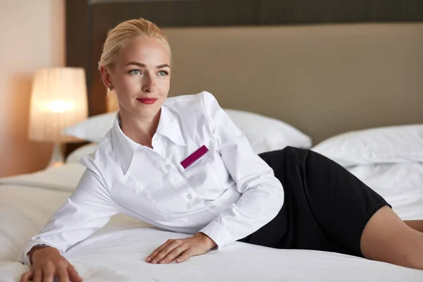 Charming chambermaid lying on white clean bed — Stock Photo, Image