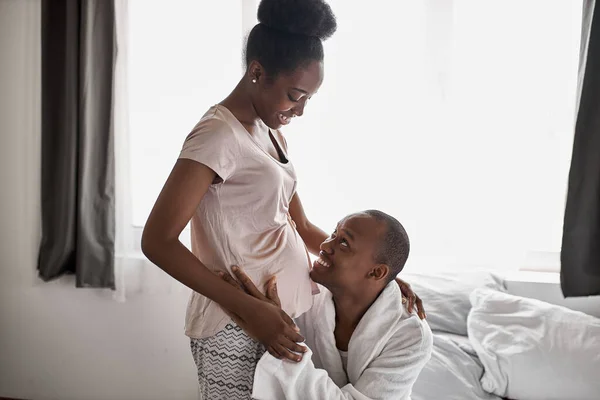 Feliz hombre africano está escuchando el vientre de su esposa embarazada — Foto de Stock