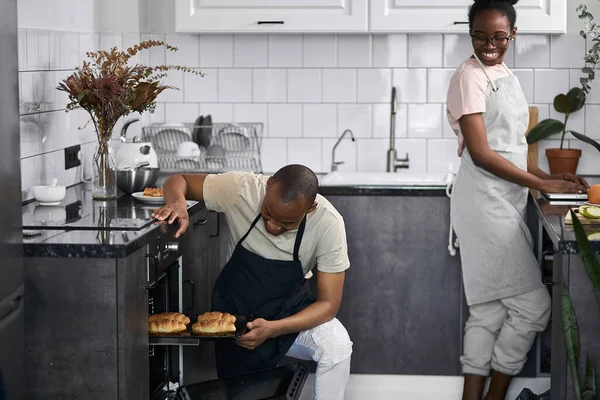 black man takes out baked goods from oven, looks whether it is ready or not